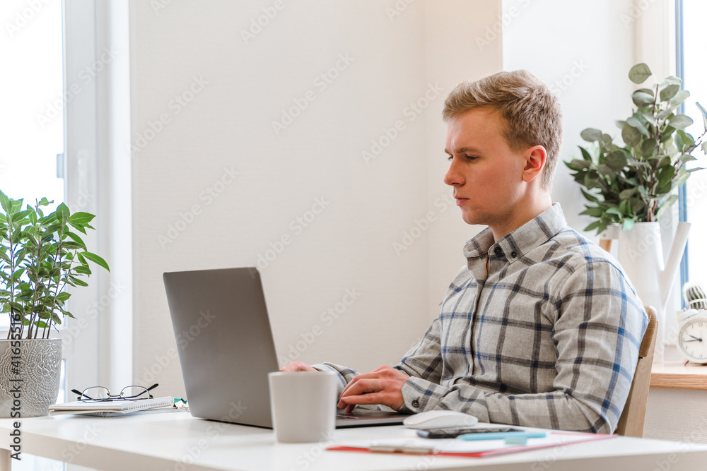 Wall mural handsome man working using computer laptop and drinking a mug of coffee with thinking serious face i