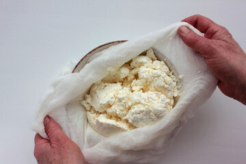 Old woman hands holding a homemade cottage cheese in cloth on white background. Ricotta cheese making process. Top view.