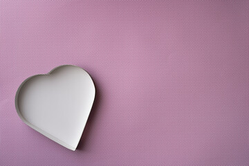 An empty, white heart-shaped box on a pink background with a pattern of small, darker pink dots. 