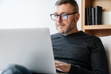 Serious adult unshaven man working with laptop while sitting at home