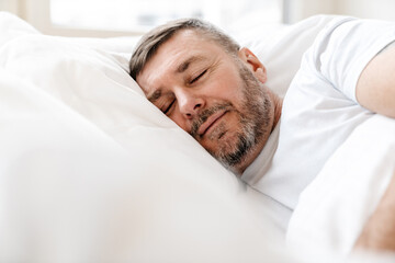 Peaceful adult unshaven man sleeping while lying in bed