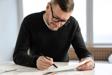 Smiling adult unshaven man working with papers at table