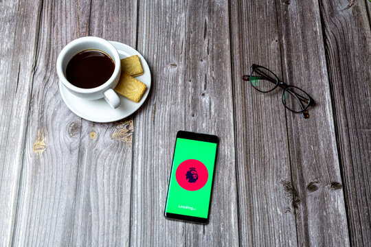 02-24-2021 Portsmouth, Hampshire, UK A Mobile Phone Or Cell Phone On A Wooden Table With The App Premier League Open Next To A Coffee And Glasses