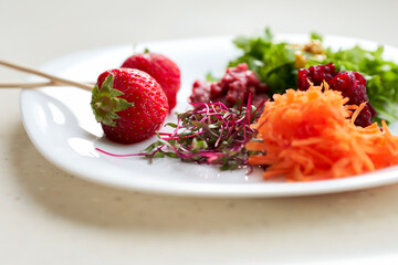  A white plate with vegetables, chard sprouts and strawberries in close-up.