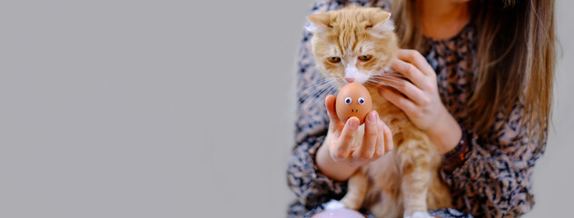 Girl holding ginger cat and funny cat looking to easter egg. Banner, copy space