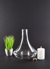 Transparent glass flask  on black background with green grass and candles