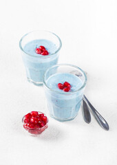 Creamy pudding with blue matcha tea, flax seeds and pomegranate seeds in a glass on a white background