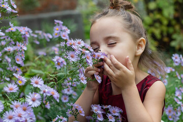 Fototapeta premium Beautiful natural smiling girl sniffing purple flowers in the forest field