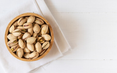 Top view of Pistachio nuts in a wooden bowl on white background