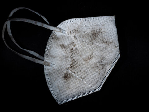 Sehr stark beschmutzte, unhygienische FFP2 Atemschutz Maske auf schwarzem Hintergrund.