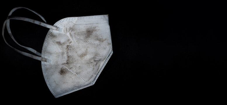 Sehr stark beschmutzte, unhygienische FFP2 Atemschutz Maske auf schwarzem Hintergrund.