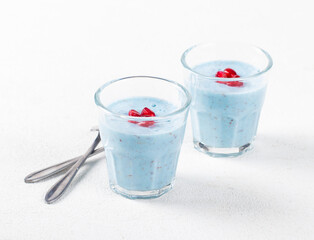 Panna Cotta with blue moth pea powder, flax seeds and pomegranate seeds in a glass on a white background