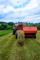 Old tractor in the field, forage harvesting for the winter, press and hay, pressing dry grass.