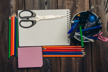 scissors lie on an open notebook and colored pencils on a wooden table top view