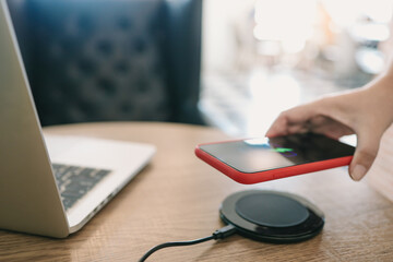 Charging mobile phone battery with wireless charging device in the table. Smartphone charging on a charging pad. Mobile phone near wireless charger Modern lifestyle concept.