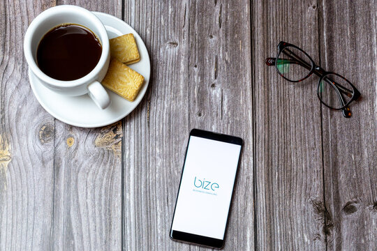 02-24-2021 Portsmouth, Hampshire, UK A mobile phone or cell phone on a wooden table with the Bize Business Emailing app open next to a coffee