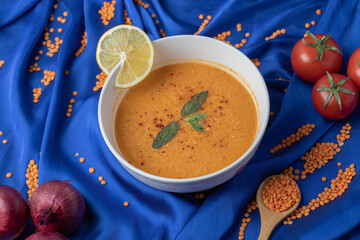 A white bowl of lentil soup with uncooked lentil beans and tomatoes