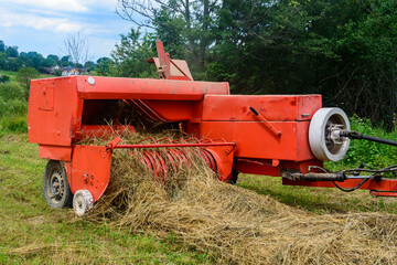 The tractor collects dry hay in the field, the hay presses the bale press, work in the field. © Niko_Dali