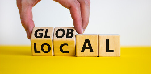 Local or global symbol. Businessman turns wooden cubes and changes the word 'local' to 'global'. Beautiful yellow table, white background. Business and local or global concept. Copy space. - obrazy, fototapety, plakaty