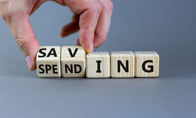 Saving or spending symbol. Businessman turns cubes and changes the word 'spending' to 'saving'. Beautiful grey table, grey background, copy space. Business and saving or spending concept.