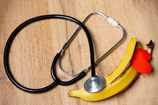 Top view. Organic,healthy food and medical concept on wooden background. Bitten banana with red paper heart shape and stethoscope for health concept. Raw vegan food and healthy life - Powered by Adobe