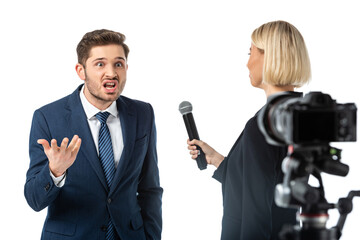 Naklejka premium blonde journalist interviewing angry businessman near digital camera on blurred foreground isolated on white