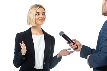 smiling blonde businesswoman talking near interviewer with microphone isolated on white