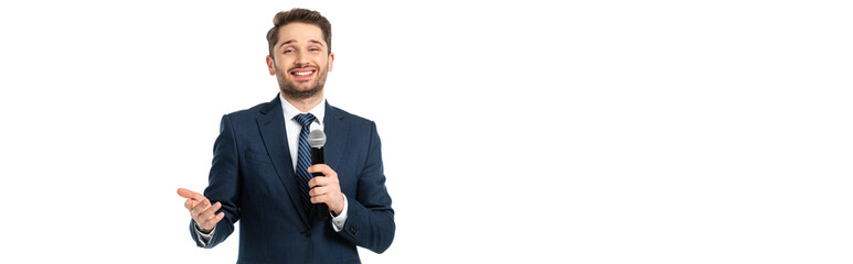 cheerful journalist with microphone pointing with hand while smiling at camera isolated on white, banner