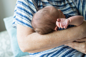 Grandmother holds newborn baby in cradle hold; grandmother wears tie-dyed blue and white shirt