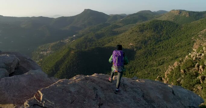 dron orbitando a una mujer escaladora con mochila de pie al borde del precipicio 