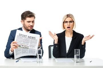 amazed news anchor gesturing near colleague reading sport news isolated on white