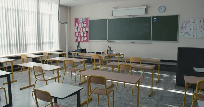 Inside view of a classroom in primary or lower secondary school. Empty classroom with chairs and desks with a chalkboard and drawings on the wall. Class without pupils, with individual school desks.