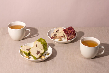 Eastern sweetness - halva with chocolate, pistachios and rose sprinkle with cups of tea on a table with a hard shadow