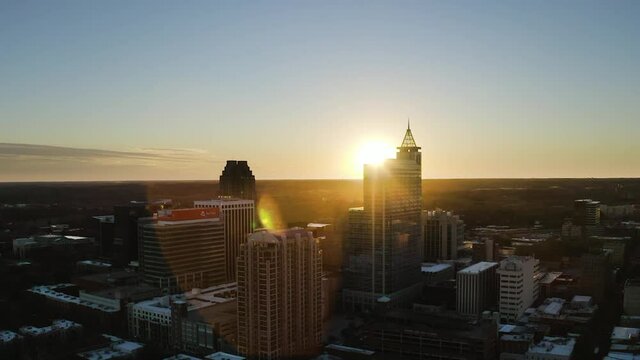Sunset at the horizon disappearing after the top of a skyscraper build from glass in downtown Raleigh on a bright sunny summer day. Wide Drone Panning shot