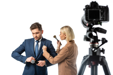 blonde makeup artist with cosmetic brush near news anchor buttoning his blazer isolated on white, blurred foreground