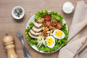 Fototapeta na wymiar Caesar salad with fried chicken, fresh tomatoes, croutons, lettuce, parmesan cheese and eggs. Healthy eating. Top view