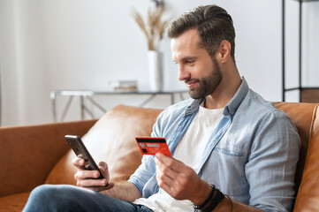Bearded hipster guy businessman, holding mobile phone and credit card for online shopping and...