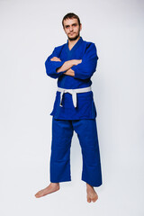 Young man in a blue kimono on a white background. The guy is a beginner in martial arts.