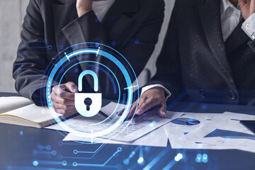 Two businesswomen working on the project to protect cyber security of international company. Padlock Hologram icons over the table with documents.