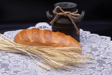Composition of white bread, wheat, an old jug on white tablecloth on black background