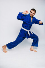 Young man in a blue kimono on a white background. The guy is a beginner in martial arts.