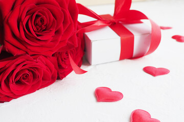 three red roses and a gift box with a bow on a white table and red hearts..