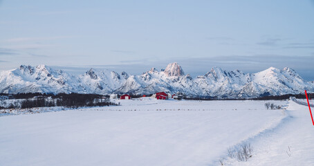 Fototapeta na wymiar Breathtaking view of Lofoten archipelago covered with snow surrounded by Norway sea. Small fishing bay with colorful houses and mountain on the background.