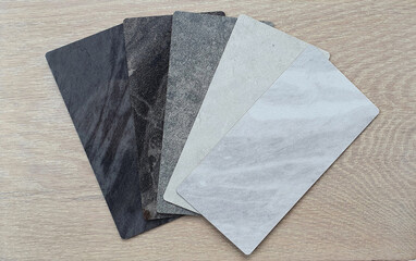 marble and stone laminated samples containing white carrara ,grey emperado ,black maquina ,beige travertine textures placed on light oak wooden background. 