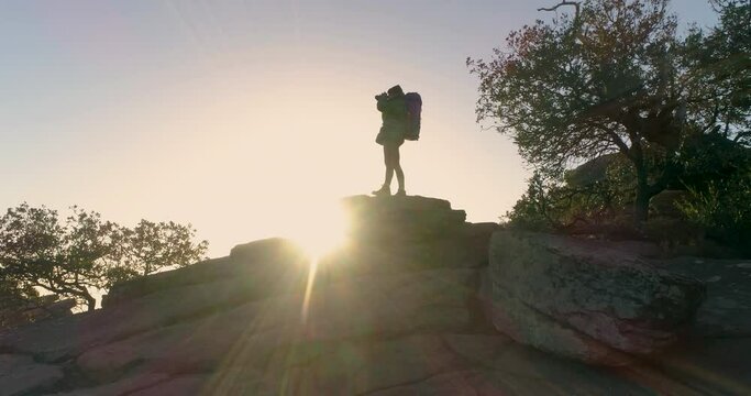 Silueta a contraluz de mujer haciendo fotograf&iacute;as al amanecer en pico de monta&ntilde;a