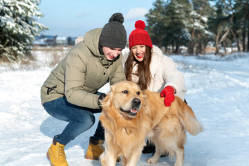 Happy young couple is played with red retriever in winter outdoors.