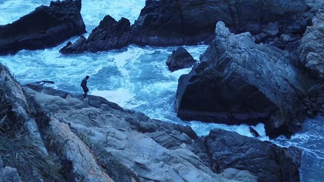 High angle view of man jumping on rocks in Punta Cometa, Mazunte, Oaxaca, Mexico, slow motion pan right