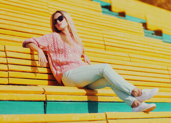 Fototapeta na wymiar Portrait of beautiful young blonde woman sitting on bench in a city park