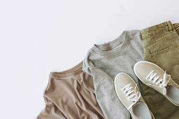 women's cappuccino-colored t-shirt, gray sweatshirt, green jeans and beige sneakers are laid out in...