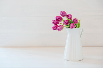 Beautiful mono bouquet of purple tulips in full bloom in white vase on white background. Copy space for text. Spring still life.